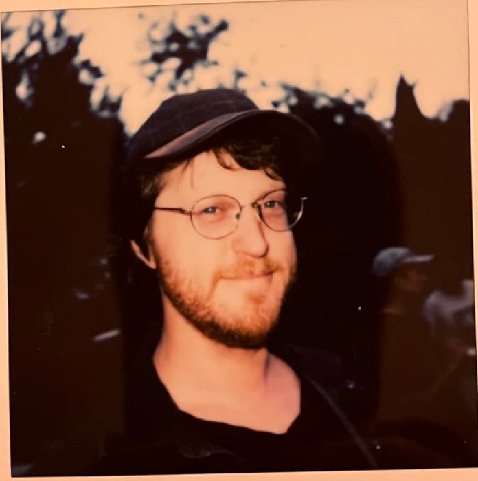 Polaroid portrait of a Byars brother in a cap and round glasses